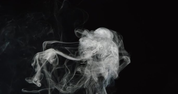 Billowing delicate smoke drifts upward into frame against black