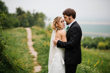 Embracing wedding couple in love on cloudy weather outdoor.
