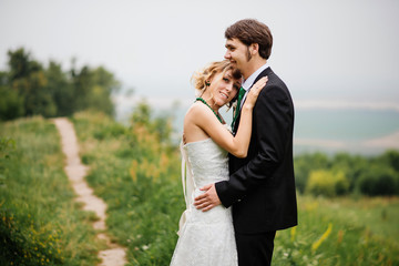 Embracing wedding couple in love on cloudy weather outdoor.