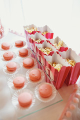 Plate with pink macaroons stands before boxes with pop-corn