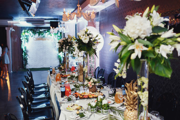 Tall vases with green and white bouquets stand on rich dinner ta