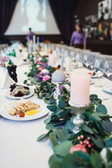 White candles on silver candleholders stand along green garland