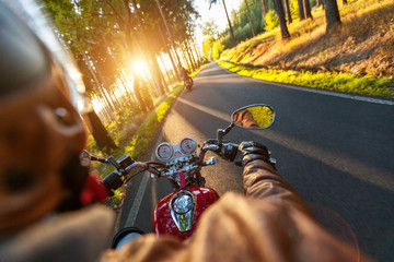 Driver riding motorcycle on an asphalt road through forest