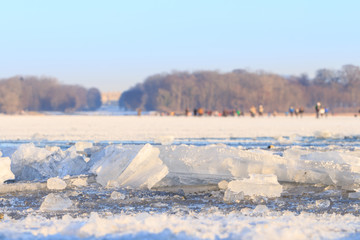 Fototapeta na wymiar closeup of Ice floes on partly frozen Lake Chiemsee on a cold winter day with Schloss Herrenchiemsee and people walking on ice blurry in background