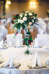 Bouquet of white roses and greenery stands in the centre of dinn