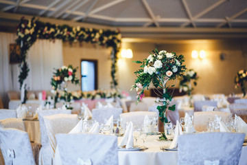 Bouquet of white roses and greenery stands in the centre of dinn