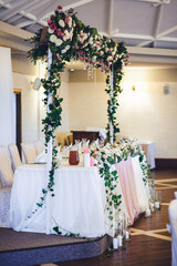 Frame with flower garland stands over dinner table prepared for