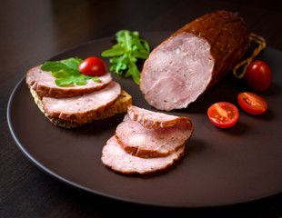 Smoked sausage, ham with red tomatoes and herbs on a dark plate