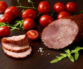 Smoked sausage, ham with red tomatoes and herbs on a dark plate