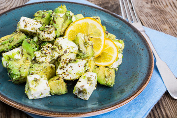 Salad with goat cheese, avocado and olive oil on wood background