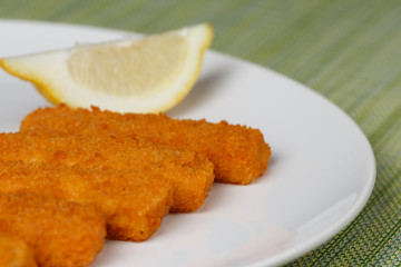 Fish fingers sticks with lemon on white plate, closeup, low focus