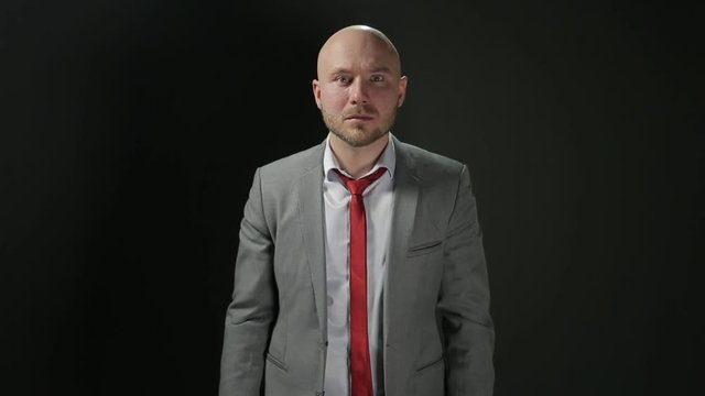 Bald man with a beard in a suit raises his head and looks at the camera with fear in his eyes. the average plan. on a black background.