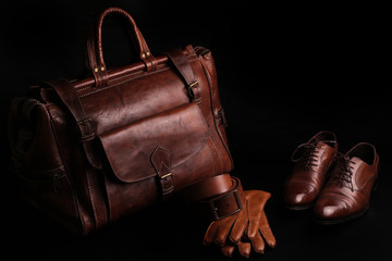 Luxury leather brown men's accessories, travel bag, belt, gloves, shoes. isolated on black background