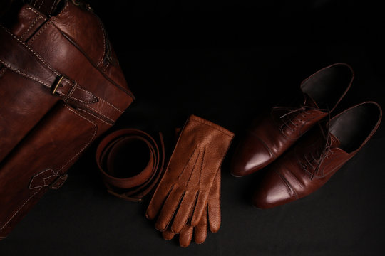 Luxury leather brown men's accessories, travel bag, belt, gloves, shoes. isolated on black background. top view