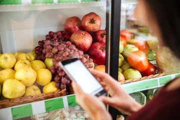 Woman choosing fruits and using cell phone in grocery shop