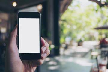 Mockup image of hand holding black mobile phone with blank white screen in loft cafe and green nature
