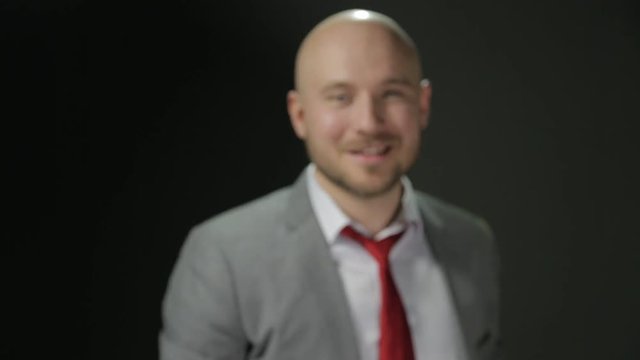 Bald man with a beard in a suit raises his head and looks at the camera with smiling and Show Big Finger Up. The close shot. on a black background.