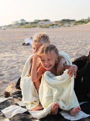 Brother and sister covered with towel at beach. Photos happy kid