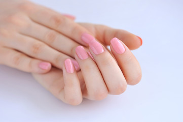 Fototapeta premium Closeup of hands of a young woman with pink manicure on nails against white background