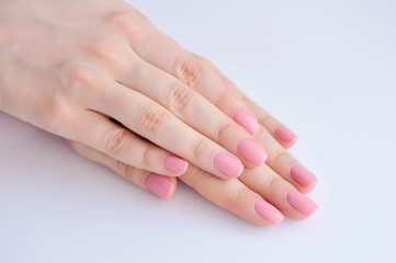 Closeup of hands of a young woman with pink manicure on nails against white background