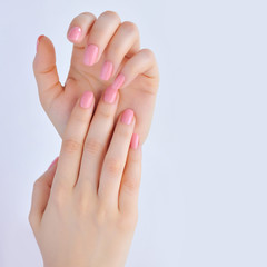 Closeup of hands of a young woman with pink manicure on nails against white background
