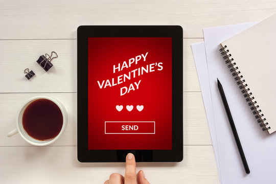 Valentine's day concept on tablet screen with office objects on white wooden table. All screen content is designed by me. Flat lay