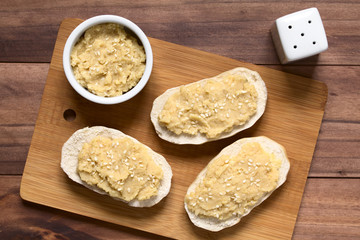 Chickpea spread or hummus on bread sprinkled with sesame seeds, photographed overhead with natural light (Selective Focus, Focus on the top of the spread on the bread and in the bowl)