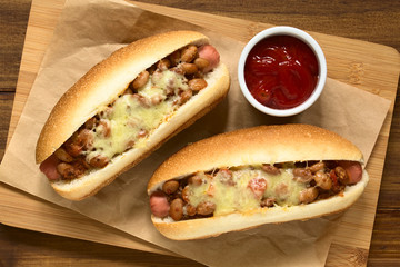 Baked chili hot dogs with ketchup on wooden board, photographed overhead with natural light