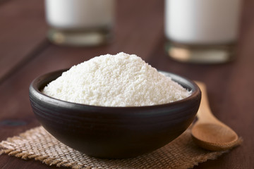 Powdered or dried milk in small bowl, photographed on dark wood with natural light (Selective Focus, Focus one third into the milk powder)