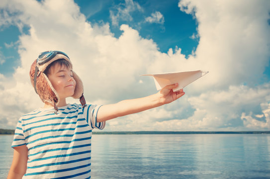 boy playing with a paper plane in aviator hat. Child on the sea in summer