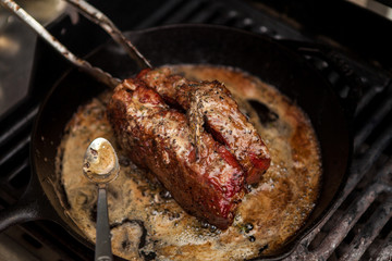 Cooking BBQ Barbecue grilling steak in a cast iron skillet with melted butter and rosemary