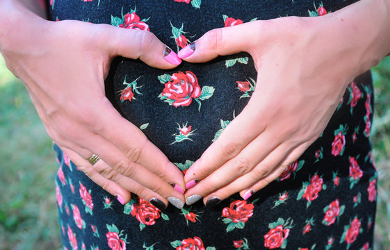 Take care of your body. The concept of a pregnancy diet. Female hands forming heart shape on belly.

