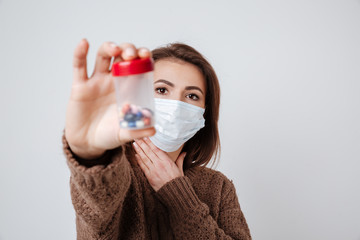 Woman in sweater and medical mask holding tablets