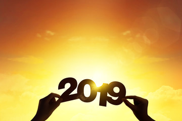 Silhouette hand holding word 2019 with lens flare blue sunset for new year concept.