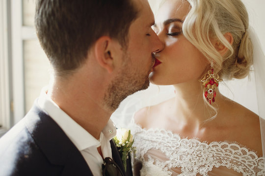 Soft kiss of gorgeous wedding couple standing in white room