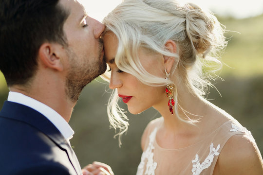 Bride bends her head to groom whil he kisses her forehead tender