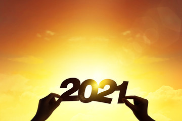 Silhouette hand holding word 2021 with lens flare blue sunset for new year concept.