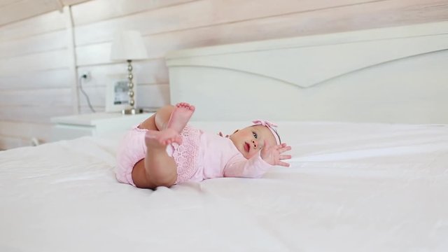 Pretty infant in pink dress lies on back on a bed at home