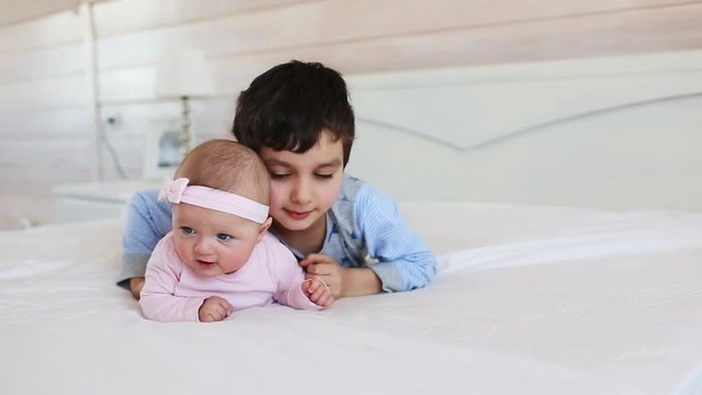 Portrait of cute brother with his little sister on a bed at home