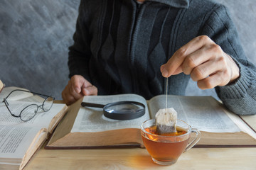 A man  brewing tea bag with glass of tea on table in reading tim