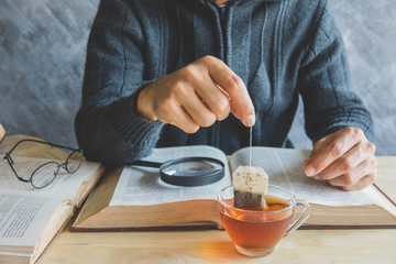 A man  brewing tea bag with glass of tea on table in reading tim