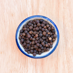 Black pepper in bowl on wood floor background.