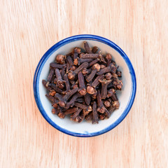 Pile cloves in bowl on wood floor background.