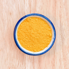 Curcuma powder in bowl on wood floor background.