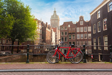 Houses and Boats on Amsterdam Canal. Morning photo of colored houses in the Dutch style and bridge with a red bicycle in the foreground - obrazy, fototapety, plakaty
