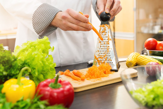 chef shredding carrots with grater in kitchen - Powered by Adobe