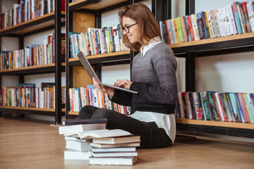 Thoughtful young woman holding and looking at the laptop