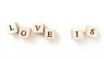 Wooden cubes with words Love Is, on white background.