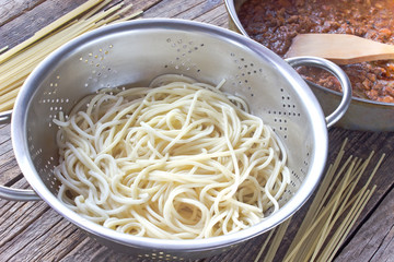 Spaghetti  pasta in strainer and bolognese sauce on table