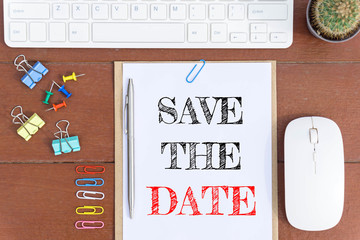 Text Save the date on white paper which has keyboard mouse pen and office equipment on wood background / business concept.